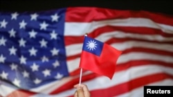 FILE - An anti-government protester holds a Taiwan national flag as a US flag flutters in the background during a demonstration to celebrate Taiwan's National Day in Hong Kong, China Oct. 10, 2019.