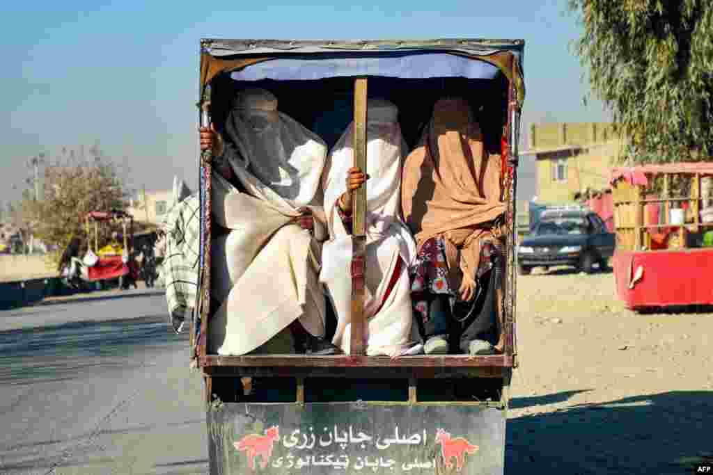 Afghan burqa-clad women ride on the back of a vehicle, in Kandahar.