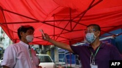 Relawan mengukur suhu tubuh seorang warga di sebuah penghalang darurat yang didirikan untuk memblokir akses ke jalan-jalan kecil di Yangon, 11 September 2020, saat diberlakukannya PSBB di wilayah tersebut. (Foto: Ye Aung THU / AFP)