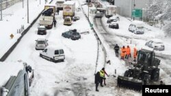 A Greek Army bulldozer plows snow next to abandoned vehicles following heavy snowfall, in Athens, Greece, Jan. 25, 2022.