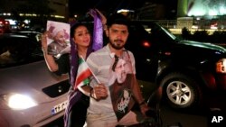 A supporter of the Iranian presidential candidate Ebrahim Raisi, right, holds his poster and the country's flag as his fiancee holds a poster of President Hassan Rouhani during a street campaign ahead the May 19 presidential election in downtown Tehran, I