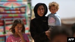 FILE - A woman who fled her village in Syria's Idlib province carries a child at a camp in Kafr Lusin near the border with Turkey, September 9, 2018.