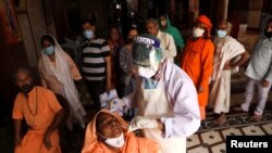 Seorang petugas kesehatan yang mengenakan alat pelindung diri mengumpulkan sampel usap dari seorang perempuan Sadhu atau perempuan suci Hindu di tengah penyebaran COVID-19, di sebuah kuil di New Delhi, India 30 Maret 2021. (Foto: Reuters)