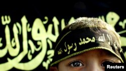 FILE - A boy stands before an Islamic jihad flag. Concern is growing in Germany and other countries that the Islamic State group, now largely weakened, is actively recruiting children to carry on their jihadist legacy. 