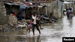 A man carries his children after Cyclone Idai at Praia Nova, in Beira, Mozambique, March 23, 2019. 
