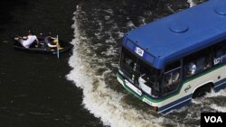 Warga mendayung perahu saat sebuah bus melintas jalanan yang tergenang air di Bangkok, Thailand (5/11).