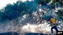 Seorang petugas pemadam kebakaran Israel memadamkan api di lapangan dekat perbatasan Israel-Gaza yang dilaporkan disebabkan oleh balon berbahan peledak yang diluncurkan dari Jalur Gaza, pada 24 Agustus 2020. (Foto: AFP)