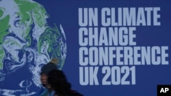 Attendees walk past a banner at the venue where COP climate conference will be held in Glasgow, Scotland, Friday, Oct. 29, 2021. The U.N. climate conference COP26 starts Sunday in Glasgow. (AP Photo/Alastair Grant)