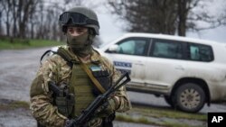 FILE - A Ukrainian soldier guards OSCE observers near the village of Shyrokyne, eastern Ukraine, April 19, 2015. 