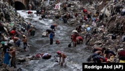 People search for scrap metal in polluted water at the bottom of one of the biggest trash dumps in the city, known as "The Mine," in Guatemala City.