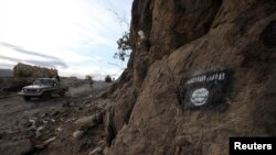 FILE - Shi'ite Houthi rebels drive a patrol truck past a Ansar al-Sharia flag painted on the side of a hill, along a road in Almnash, the main stronghold of Ansar al-Sharia, the local wing of al-Qaeda in the Arabian Peninsula (AQAP), in Rada, Nov. 22, 2014. 