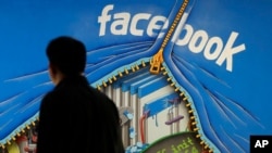 FILE - A man walks past a mural in an office on the Facebook campus in Menlo Park, Calif., June 11, 2014.