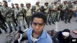 An Egyptian protester boy stands in front of army soldiers who try to lead the protesters away from Tahrir Square in Cairo, Egypt Sunday morning, Feb. 13, 2011. Egypt's military took down the makeshift tents of protesters who camped out on the square in a