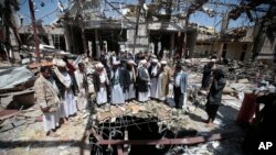 FILE- In this Oct. 13, 2016 file photo, members of the Higher Council for Civilian Community Organization inspect a destroyed funeral hall as they protest against a deadly Saudi-led airstrike on a funeral hall six days ago, in Sana'a, Yemen. 