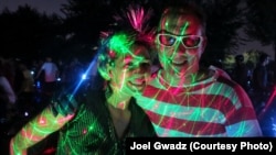 D.C. Bike Party riders are lit up by disco ball lights. They stand among Japanese cherry trees in a local park.