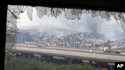 A window shattered by the shockwaves frames the site of an explosion at a warehouse in northeastern China's Tianjin municipality, Aug. 14, 2015. 
