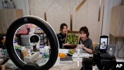 In this May 5, 2020, photo, China's online celebrity Zhang Mofan, right, introduces fresh mangos to her online clients and fans through the live-streaming at her house in Beijing. 