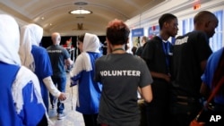 In this July 17, 2017, photo, members of the Afghanistan team, left, walk past two Burundi team members, at right in black shirts, during the FIRST Global Robotics Challenge in Washington.