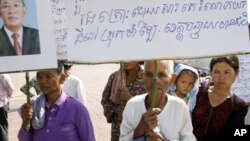 Sam Souen, an 86 year-old Cambodian woman, holds a banner asking Prime Minister Hun Sen, seen in photo at left, to help solve the problem of land grabbing, file photo. 