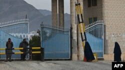 Women wearing a burqa walk toward the main gate of Laghman University as Taliban fighters stand guard in Mihtarlam, Laghman province, Feb. 2, 2022.