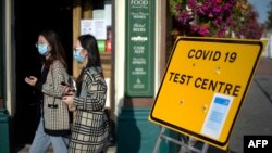 Pedestrians wearing facemasks walks past a sign for a Covid-19 test centre in Leyton, east London on September 19, 2020. (Photo by DANIEL LEAL-OLIVAS / AFP)