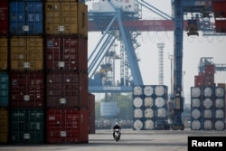 Seorang pekerja mengendarai sepeda motor melewati tumpukan peti kemas di Terminal Peti Kemas IPC Pelabuhan Tanjung Priok, Jakarta, 4 November 2021. (Foto: REUTERS/Willy Kurniawan)