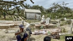 Relatives sit next to bodies exhumated from graves destroyed by Cyclon Batsirai at the local cemetery in Mahanoro, Madagascar, Feb. 6, 2022.