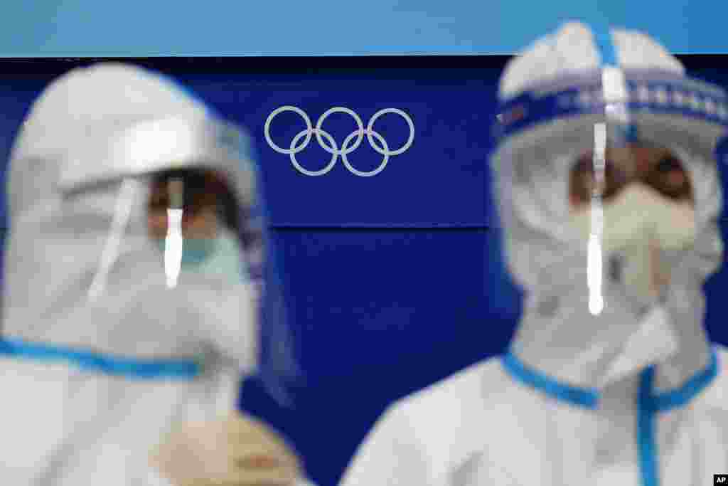 The Olympic rings are seen behind workers in protective equipment at the National Indoor Stadium, Feb. 1, 2022.
