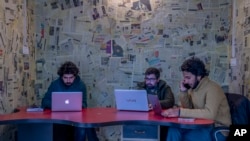 FILE- Fahad Shah, right, editor-in-chief of Kashmir Walla, works on his computer inside the newsroom at his office in Srinagar, Indian controlled Kashmir, Jan. 21, 2022. Shah was arrested in February under India's anti-terror law. 