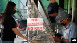 FILE - A woman stands beside a sign to remind passengers to show their vaccination card before riding at a jeepney terminal in Quezon city, Philippines on Jan. 17, 2022.