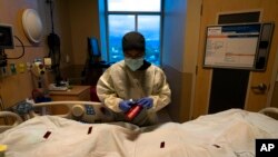 FILE - A nurse attaches a 'COVID Patient' sticker to the body bag of a patient who died of coronavirus at Providence Holy Cross Medical Center in Los Angeles, on Dec. 14, 2021.