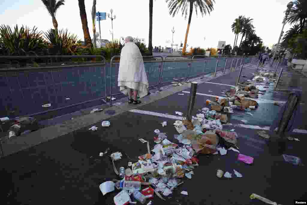 A man walks through debris scatterd on the street the day after a truck ran into a crowd at high speed killing scores celebrating the Bastille Day July 14 national holiday on the Promenade des Anglais in Nice, France, July 15, 2016.