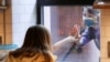 FILE - Friends say hello through a kitchen window during the outbreak of the coronavirus disease in Brooklyn, New York, May 17, 2020.