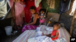 អ្នកស្រី Roselia Jean Charles មើលកូនស្រីរបស់គាត់យំនៅក្នុងខ្ទមដែលជាផ្ទះរបស់ពួកគេនៅឯជំរុំ Devirel ប្រាំមួយខែបន្ទាប់ពីការរញ្ជួយដីកម្រិត 7.2 នៅទីក្រុង Les Cayes ប្រទេសហៃទី ថ្ងៃទី 16 ខែកុម្ភៈ ឆ្នាំ 2022។