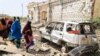 Women walk past a destroyed house and the wreckage of a car following an attack by Al-Shabaab militant to a police station on the outskirts of Mogadishu, Somalia, Feb. 16, 2022. 
