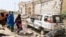 Women walk past a destroyed house and the wreckage of a car following an attack by Al-Shabaab militant to a police station on the outskirts of Mogadishu, Somalia, Feb. 16, 2022. 