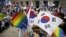An activist holds up a rainbow-colored fan and a South Korean national flag as gay pride festival participants face Christians opposed to homosexuality in central Seoul, South Korea, June 28, 2015.