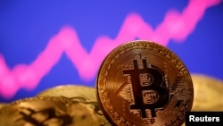FILE - A representation of virtual currency bitcoin is seen in front of a stock graph in this photo illustration created Jan. 8, 2021. The value of bitcoin, the most popular form of cryptocurrency, has dropped more than 70% since its peak in November of last year.