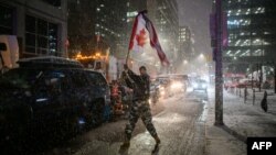 Snow falls around a demonstrator waving a flag during a protest by truck drivers over pandemic health rules and the Trudeau government, outside the parliament of Canada in Ottawa on Feb. 17, 2022.