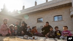 FILE - Milhem Daher, 35, drinks tea as he sits with his family outside his house in the village of Kasrat Srour, in the southeastern countryside of the Raqqa province, Syria, Feb. 7, 2022.