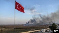 Asap membubung dari Tal Abyad, sebuah kota di Suriah. Foto diambil dari perbatasan Turki di mana tampak bendera Turki di Akcakale, 10 Oktober 2019. 