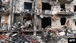 Petugas pemadam kebakaran bekerja di sebuah bangunan tempat tinggal yang rusak di Jalan Koshytsa, pinggiran Ibu Kota Ukraina Kyiv, di mana sebuah peluru militer diduga menghantam, pada 25 Februari 2022. (Foto: AFP)