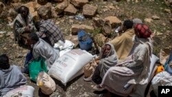 FILE - An elderly Ethiopian woman sits with others next to a sack of wheat donated to conflict victims in the town of Agula, in the Tigray region of northern Ethiopia, May 8, 2021.