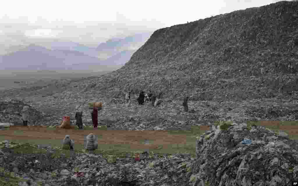 FILE - People who scavenge recyclable materials from garbage for a living walk near a mountain of garbage at the dump on the outskirts of Kabul, Afghanistan, Dec. 11, 2018.