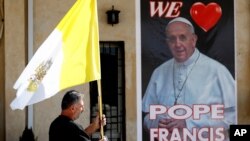 Seorang Pastor memegang bendera di dekat poster Paus Fransiskus, dalam persiapan menjelang kunjungan Paus di gereja Mar Youssif Church, Baghdad, Irak (26/2). 
