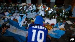 A fan mourns in front of flowers and posters left in tribute to Diego Maradona at the entrance of the Boca Juniors stadium known as La Bombonera in Buenos Aires, Argentina, Nov. 27, 2020. Maradona died Nov. 25 at age 60.