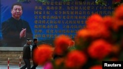 បុរសៗ​ដើរ​កាត់​ផ្ទាំង​រូប​របស់​លោក​ប្រធានាធិបតី Xi Jinping នៅ​ថ្ងៃទី២ នៃ​ការ​ប្រជុំ​ពេញ​អង្គ​នៃ​គណៈកម្មាធិការ​កណ្តាល​នៃ​គណបក្ស​កុម្មុយនិស្ត​ចិន​ទី១៨ ក្នុង​ក្រុង​ប៉េកាំង កាលពី​ថ្ងៃទី២៥ ខែតុលា ឆ្នាំ២០១៦។