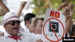 FILE - A taxi driver holds a sign which reads "No Uber, out" during a protest against car-sharing service Uber, outside the embassy of Colombia, in San Jose.