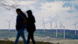 People are silhouetted as they stroll past power generating wind turbines visible from a walking path at the Flight 93 National Memorial in Shanksville, Pa., Saturday, May 8, 2021. (AP Photo/Keith Srakocic)