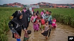FILE - Rohingya Muslims, who crossed over from Myanmar into Bangladesh, wade past a waterlogged path leading to the Jamtoli refugee camp in Ukhiya, Bangladesh, Nov. 17, 2017.